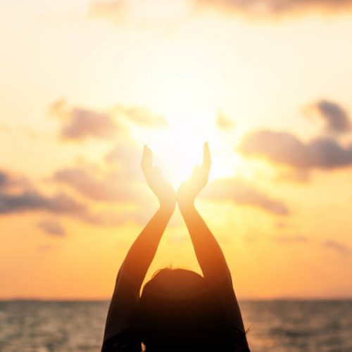 istockphoto-976509990-612×612 Summer sun solstice concept and silhouette of happy young womanâs hands relaxing, meditating and holding sunset against warm golden hour sky on the beach with ocean or sea background
